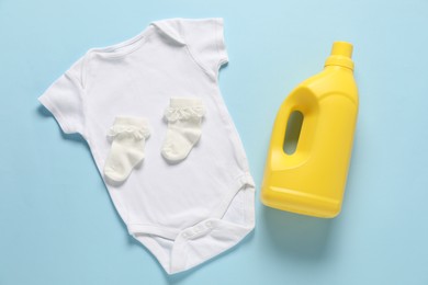 Photo of Bottle of fabric softener and baby clothes on light blue background, flat lay