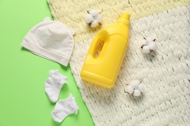 Photo of Bottle of fabric softener, baby clothes, blanket and cotton flowers on green background, flat lay