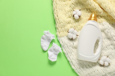 Photo of Bottle of fabric softener, baby socks, blanket and cotton flowers on green background, flat lay. Space for text
