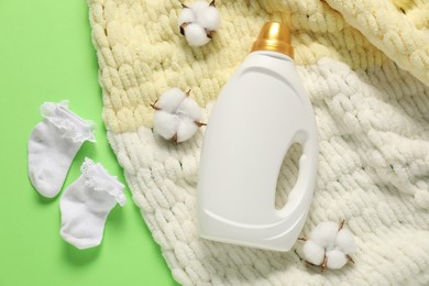 Photo of Bottle of fabric softener, baby socks, blanket and cotton flowers on green background, flat lay
