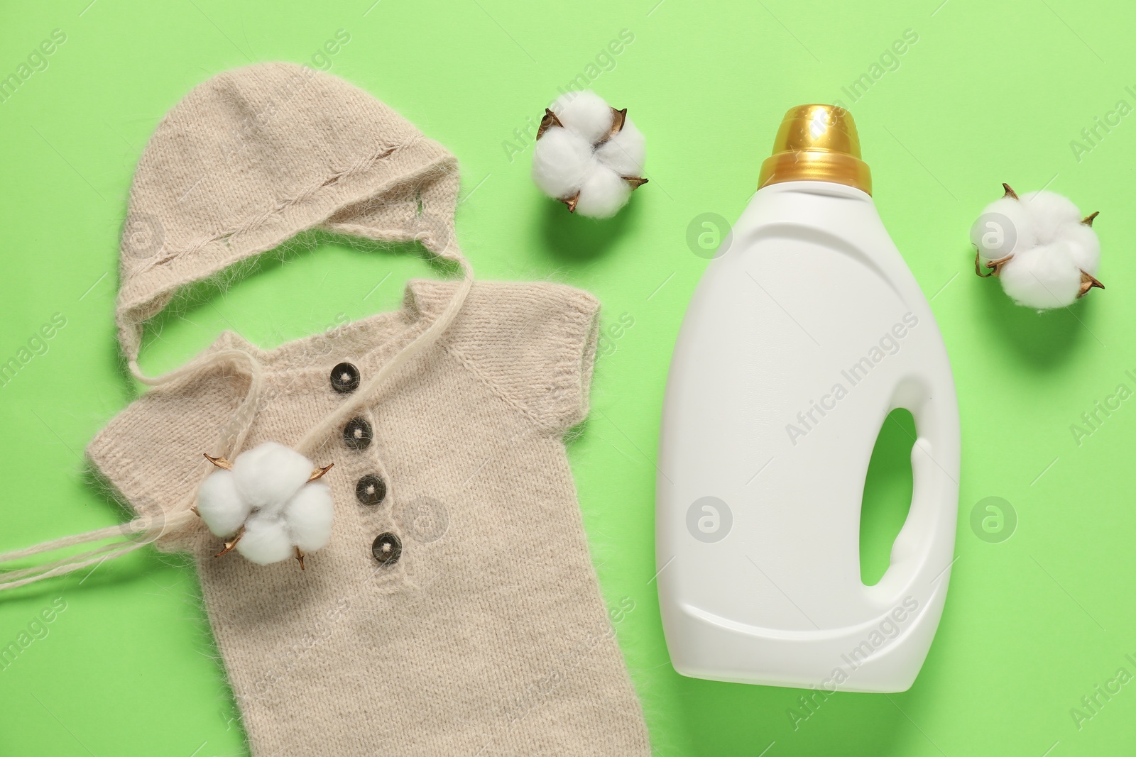Bottle of fabric softener, cotton flowers and baby clothes on green background, flat lay Photo of Bottle of fabric softener, cotton flowers and baby clothes on green background, flat lay