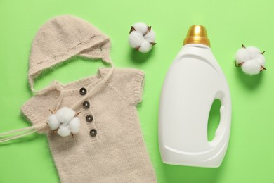 Photo of Bottle of fabric softener, cotton flowers and baby clothes on green background, flat lay