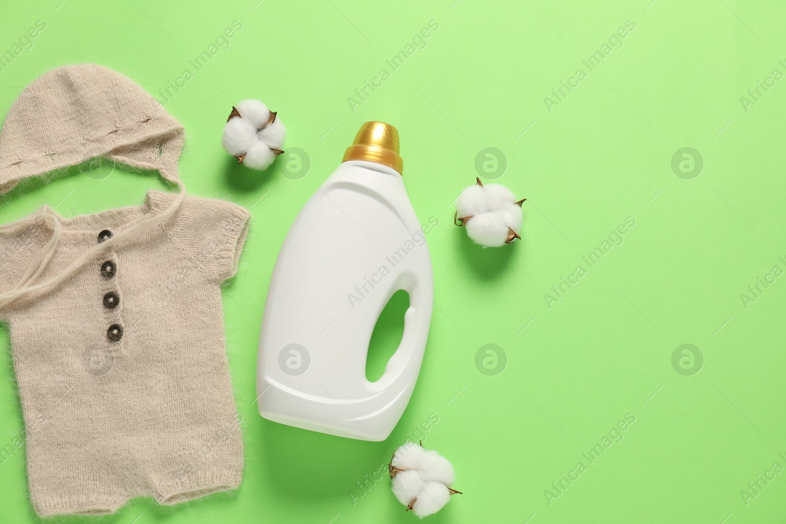 Bottle of fabric softener, cotton flowers and baby clothes on green background, flat lay. Space for text Photo of Bottle of fabric softener, cotton flowers and baby clothes on green background, flat lay. Space for text