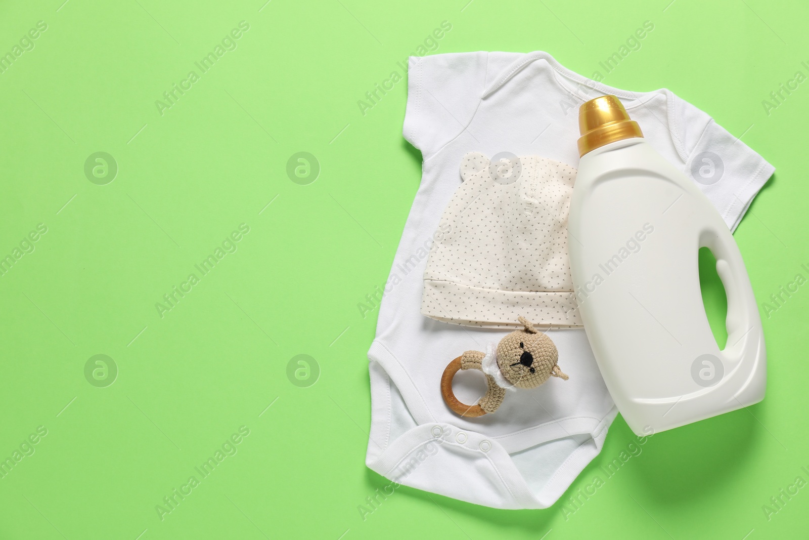 Bottle of fabric softener, toy and baby clothes on green background, flat lay. Space for text Photo of Bottle of fabric softener, toy and baby clothes on green background, flat lay. Space for text