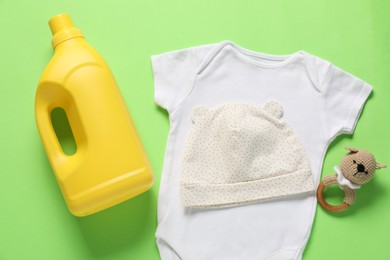 Photo of Bottle of fabric softener, toy and baby clothes on green background, flat lay