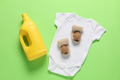 Photo of Bottle of fabric softener and baby clothes on green background, flat lay