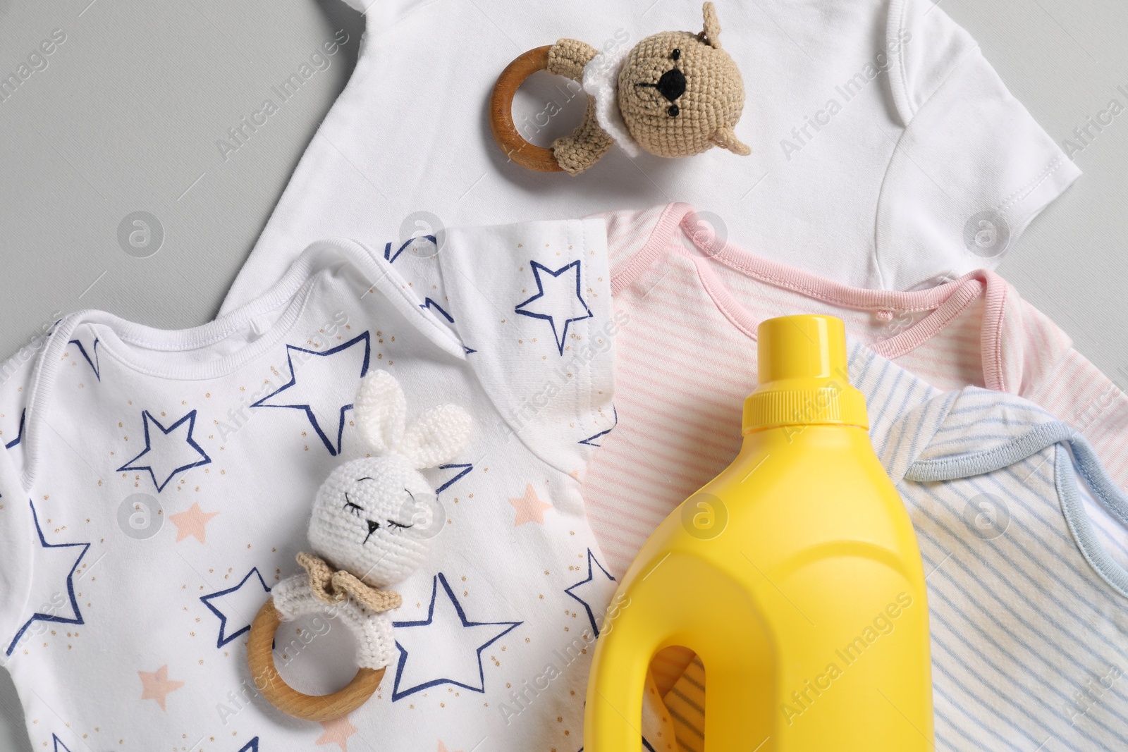 Bottle of fabric softener, toys and baby clothes on light grey background, flat lay Photo of Bottle of fabric softener, toys and baby clothes on light grey background, flat lay