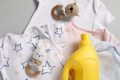 Photo of Bottle of fabric softener, toys and baby clothes on light grey background, flat lay