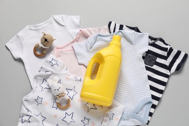 Photo of Bottle of fabric softener, toys and baby clothes on light grey background, flat lay