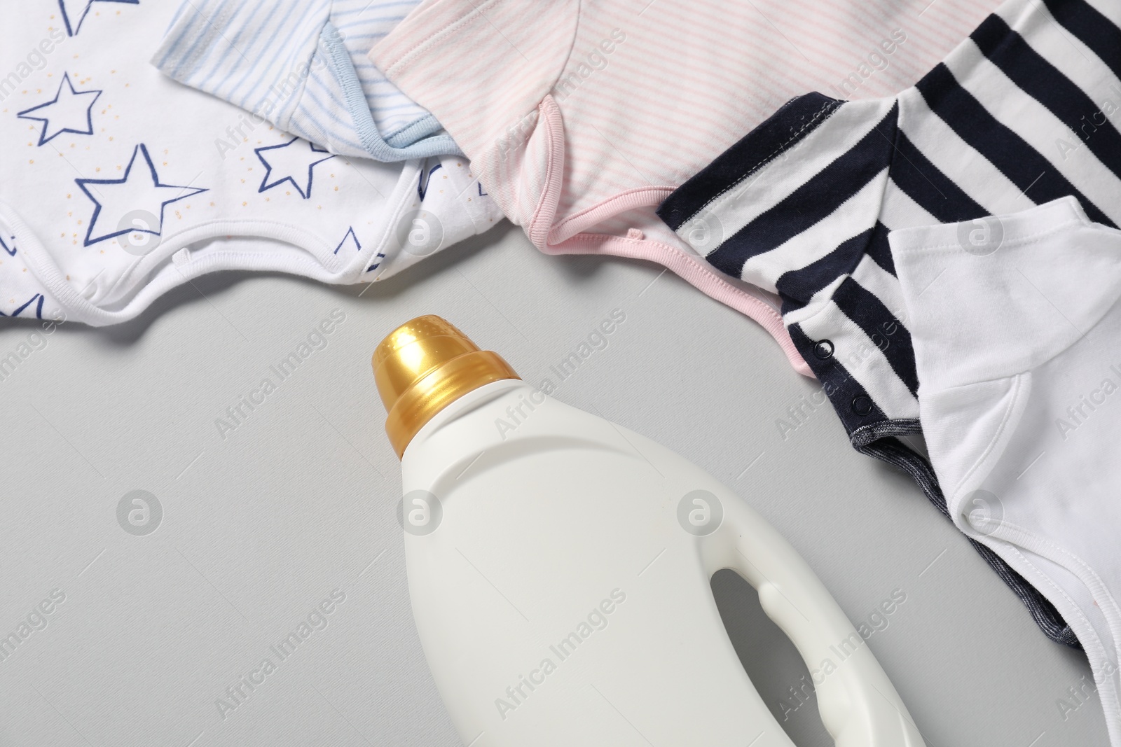 Bottle of fabric softener and baby clothes on light grey background, closeup Photo of Bottle of fabric softener and baby clothes on light grey background, closeup