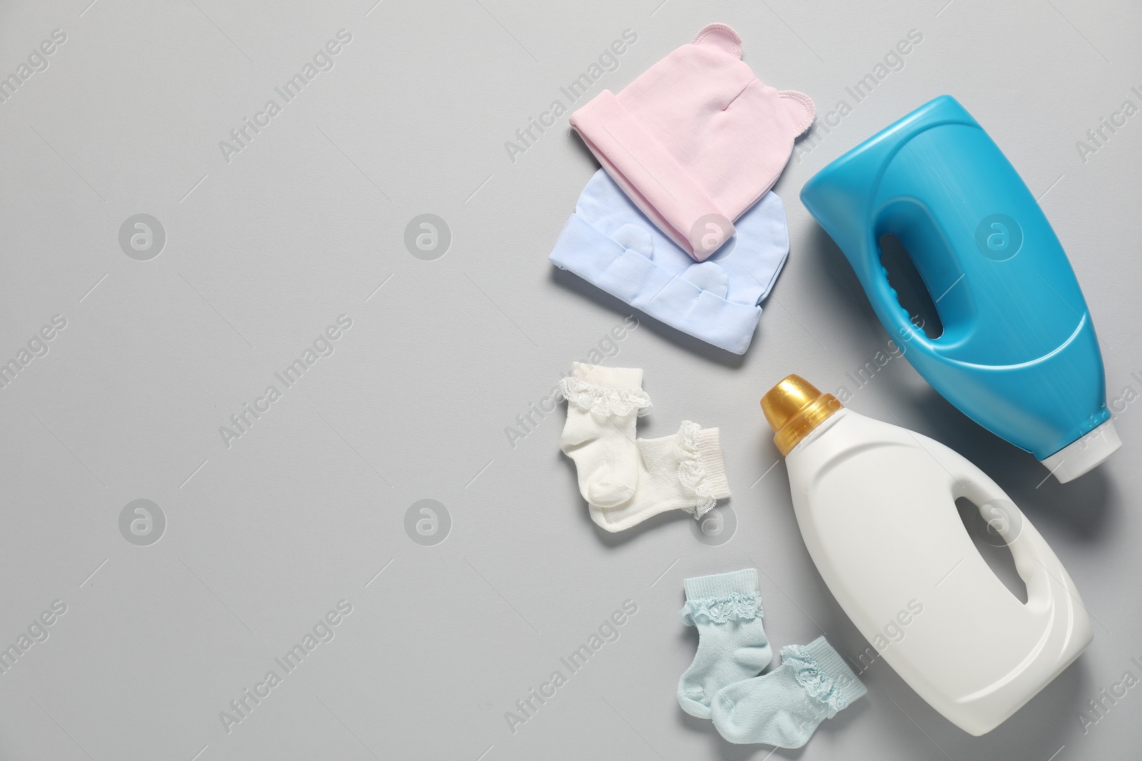 Bottles of fabric softener and baby clothes on light grey background, flat lay. Space for text Photo of Bottles of fabric softener and baby clothes on light grey background, flat lay. Space for text