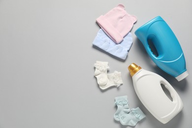 Photo of Bottles of fabric softener and baby clothes on light grey background, flat lay. Space for text