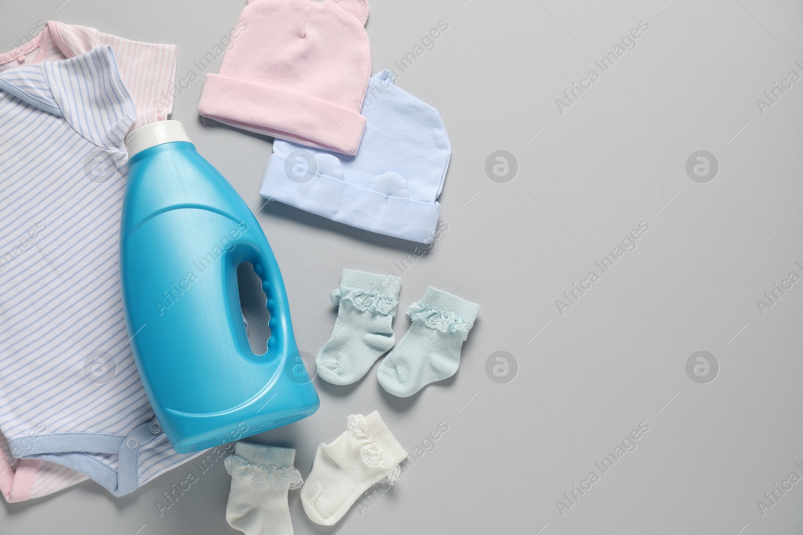 Bottle of fabric softener and baby clothes on light grey background, flat lay. Space for text Photo of Bottle of fabric softener and baby clothes on light grey background, flat lay. Space for text