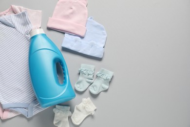 Photo of Bottle of fabric softener and baby clothes on light grey background, flat lay. Space for text