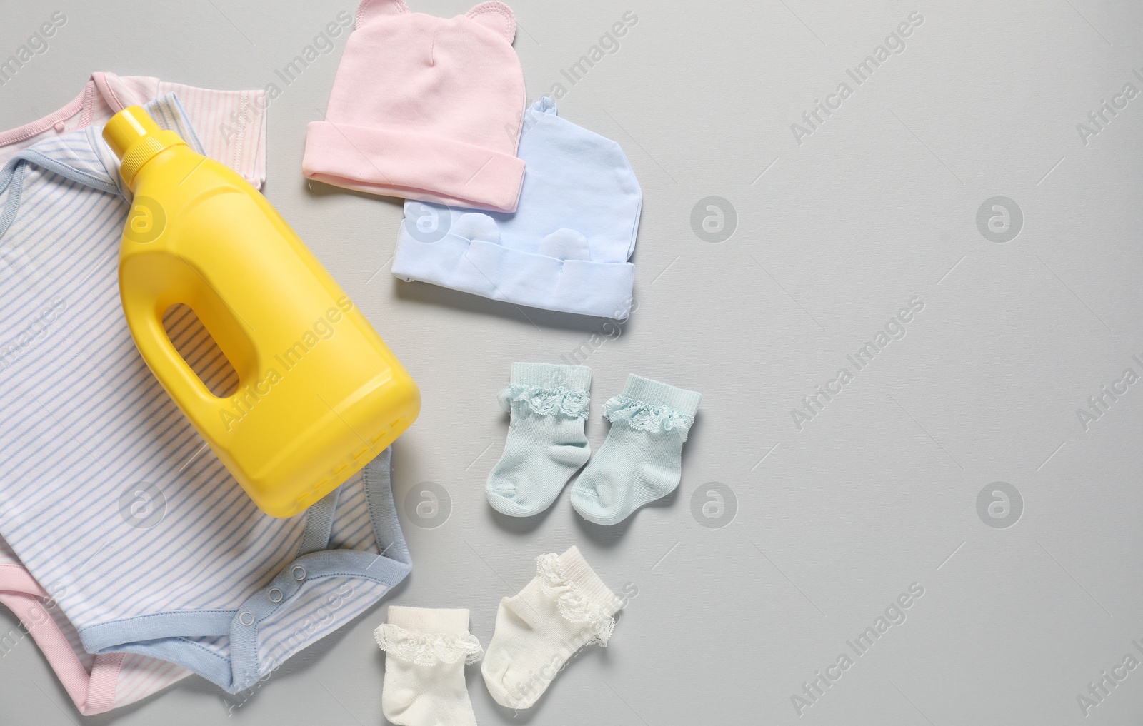 Bottle of fabric softener and baby clothes on light grey background, flat lay. Space for text Photo of Bottle of fabric softener and baby clothes on light grey background, flat lay. Space for text