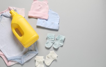 Photo of Bottle of fabric softener and baby clothes on light grey background, flat lay. Space for text