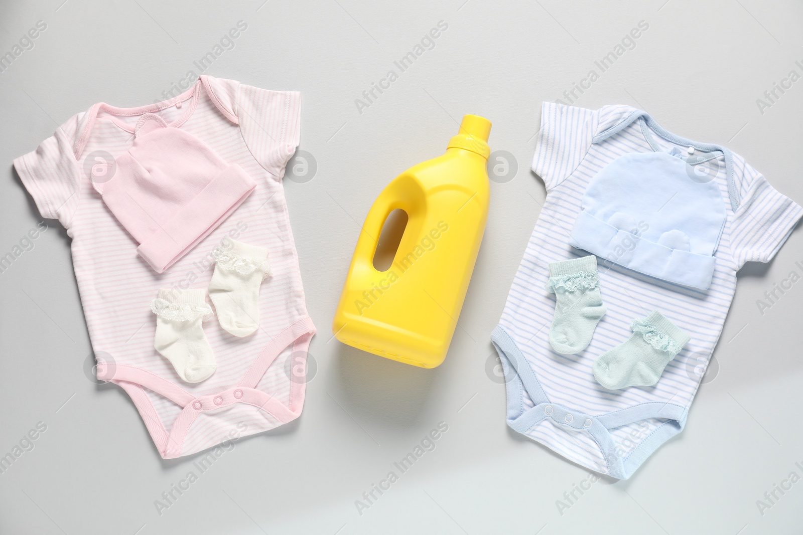 Bottle of fabric softener and baby clothes on light grey background, flat lay Photo of Bottle of fabric softener and baby clothes on light grey background, flat lay