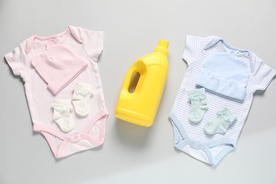 Photo of Bottle of fabric softener and baby clothes on light grey background, flat lay