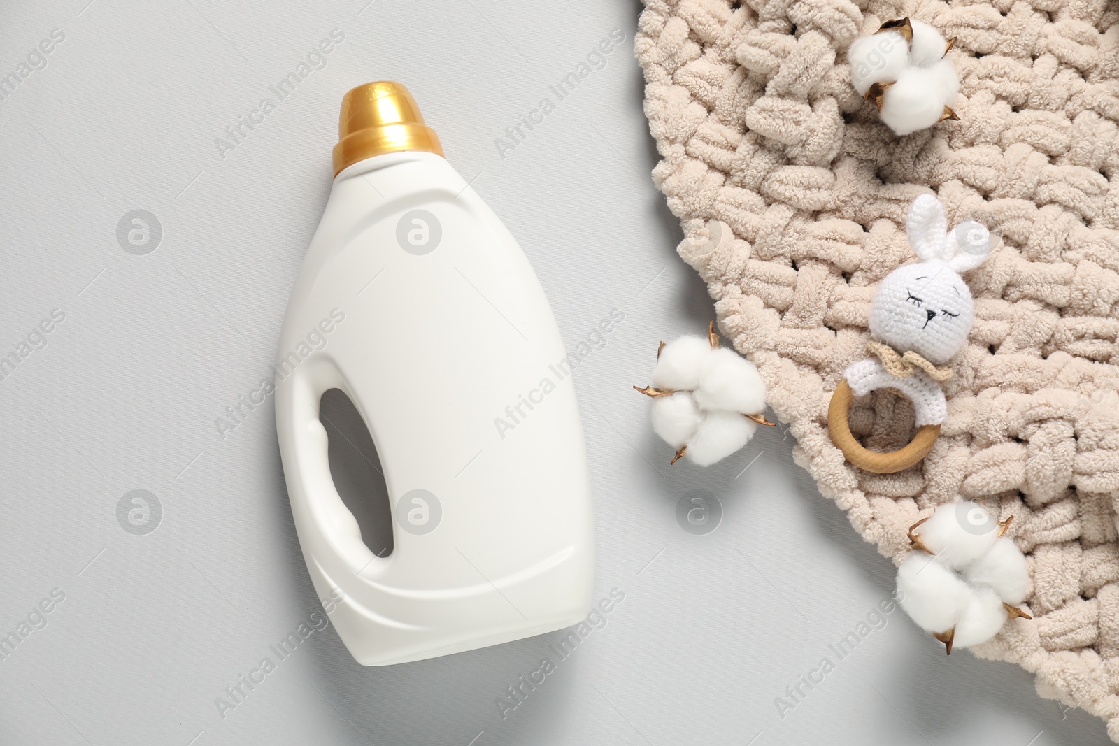 Bottle of fabric softener, toy, baby blanket and cotton flowers on light grey background, flat lay Photo of Bottle of fabric softener, toy, baby blanket and cotton flowers on light grey background, flat lay