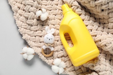 Photo of Bottle of fabric softener, toy, baby blanket and cotton flowers on light grey background, flat lay