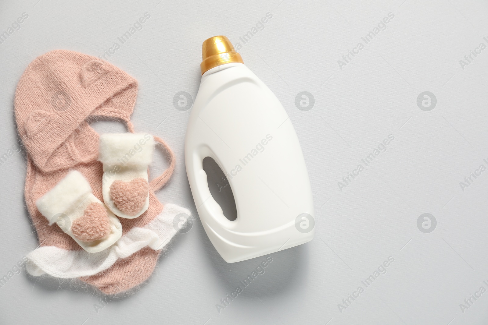 Bottle of fabric softener and baby clothes on light grey background, flat lay. Space for text Photo of Bottle of fabric softener and baby clothes on light grey background, flat lay. Space for text