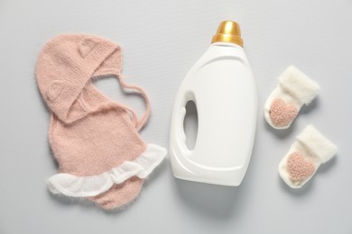Photo of Bottle of fabric softener and baby clothes on light grey background, flat lay