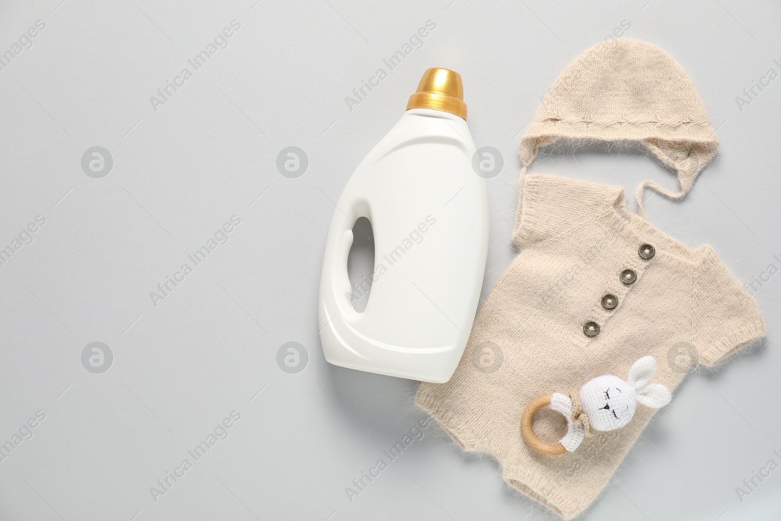Bottle of fabric softener, toy and baby clothes on light grey background, flat lay. Space for text Photo of Bottle of fabric softener, toy and baby clothes on light grey background, flat lay. Space for text