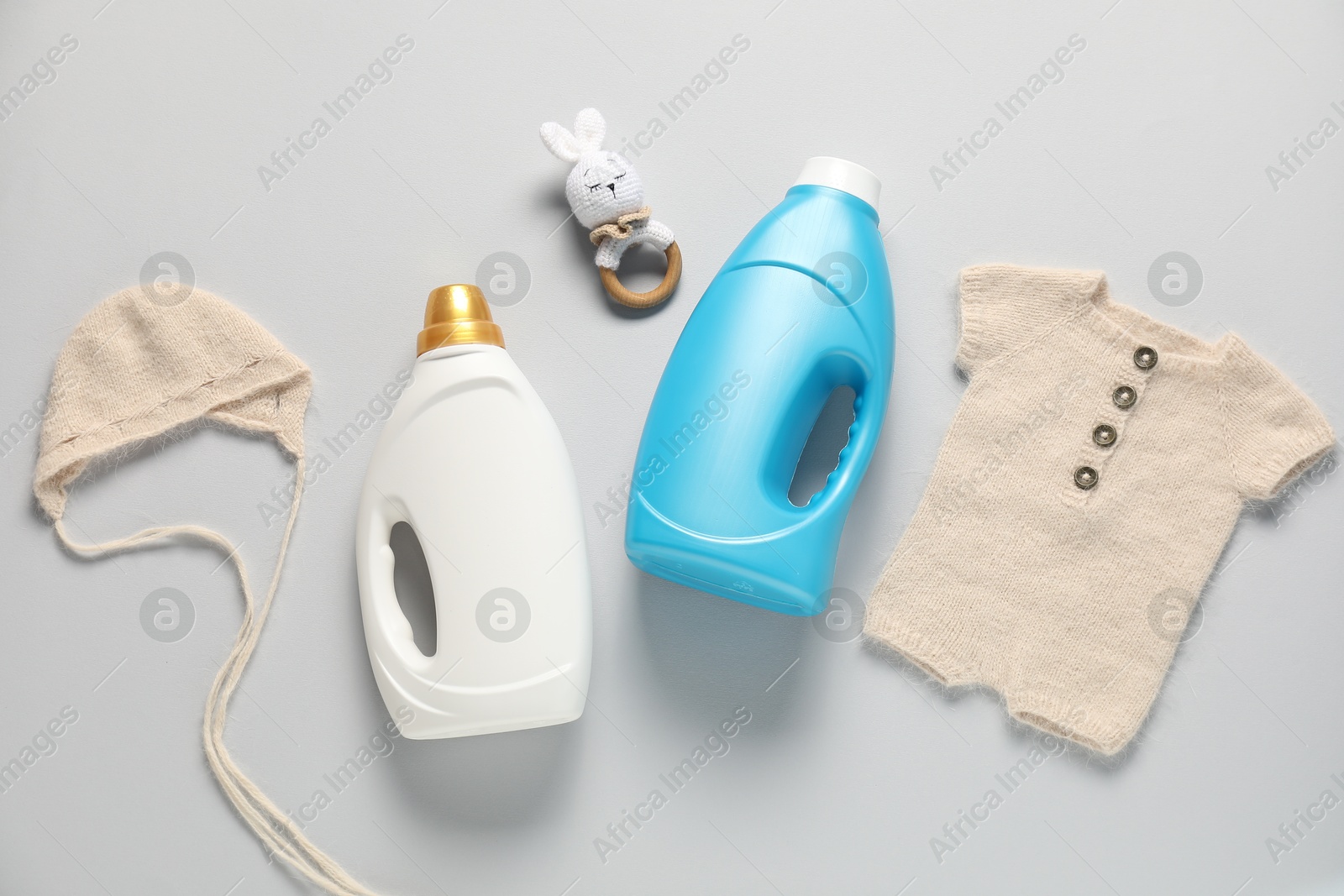 Bottles of fabric softener, toy and baby clothes on light grey background, flat lay Photo of Bottles of fabric softener, toy and baby clothes on light grey background, flat lay