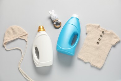 Photo of Bottles of fabric softener, toy and baby clothes on light grey background, flat lay