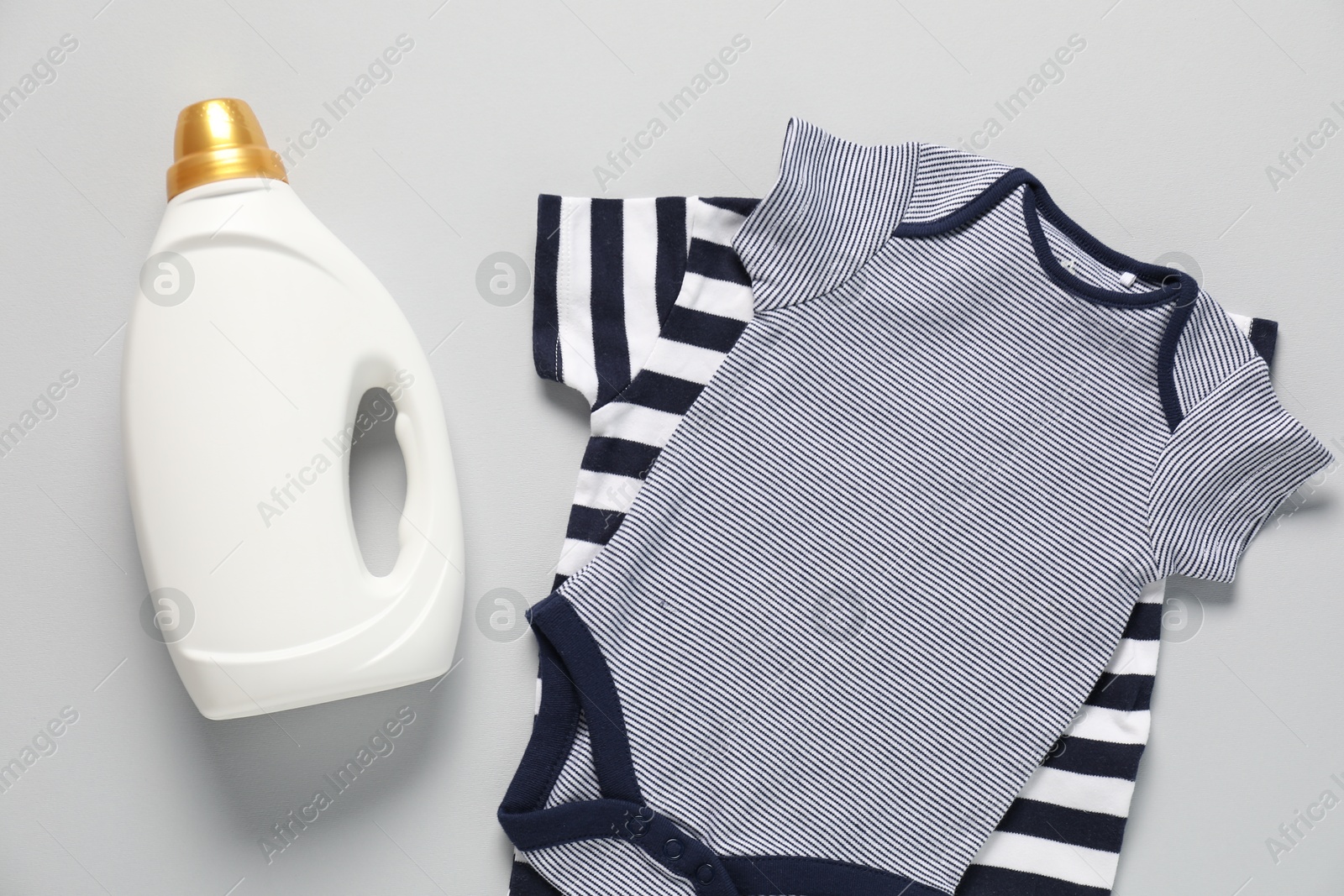Bottle of fabric softener and baby clothes on light grey background, flat lay Photo of Bottle of fabric softener and baby clothes on light grey background, flat lay
