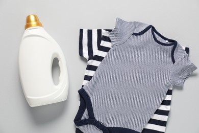 Photo of Bottle of fabric softener and baby clothes on light grey background, flat lay
