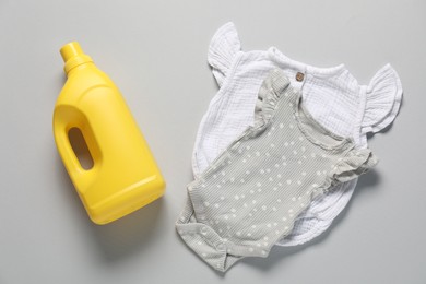 Photo of Bottle of fabric softener and baby clothes on light grey background, flat lay