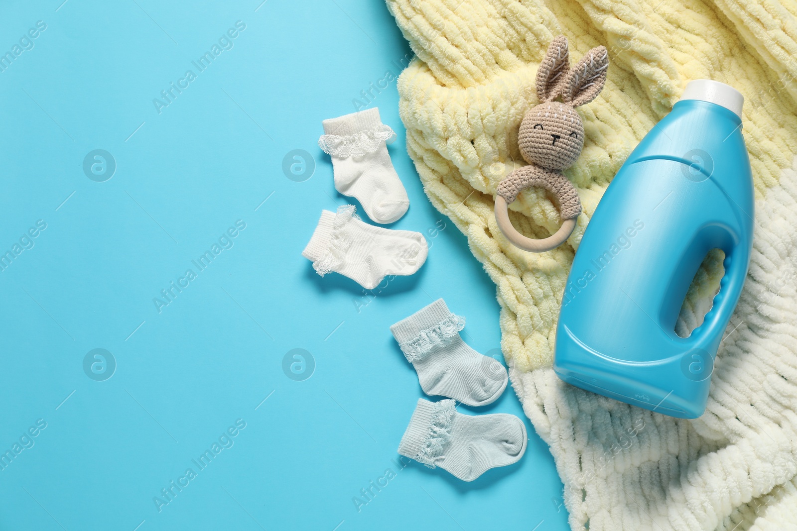 Bottle of fabric softener, toy, baby socks and blanket on light blue background, flat lay. Space for text Photo of Bottle of fabric softener, toy, baby socks and blanket on light blue background, flat lay. Space for text