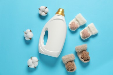 Photo of Bottle of fabric softener, cotton flowers and baby socks on light blue background, flat lay
