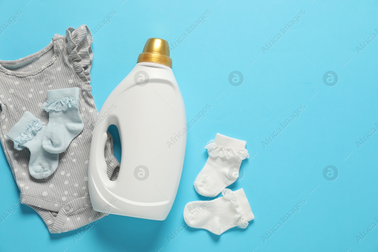 Bottle of fabric softener and baby clothes on light blue background, flat lay. Space for text Photo of Bottle of fabric softener and baby clothes on light blue background, flat lay. Space for text