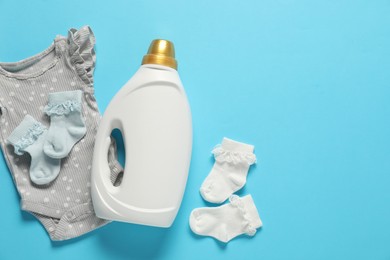 Photo of Bottle of fabric softener and baby clothes on light blue background, flat lay. Space for text