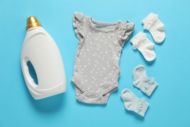 Photo of Bottle of fabric softener and baby clothes on light blue background, flat lay