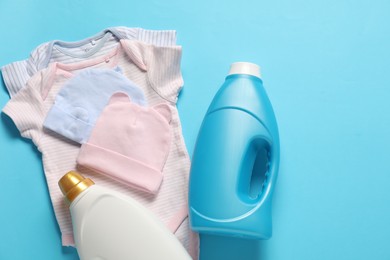 Photo of Bottles of fabric softener and baby clothes on light blue background, flat lay