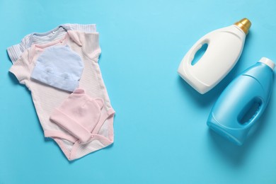 Photo of Bottles of fabric softener and baby clothes on light blue background, flat lay