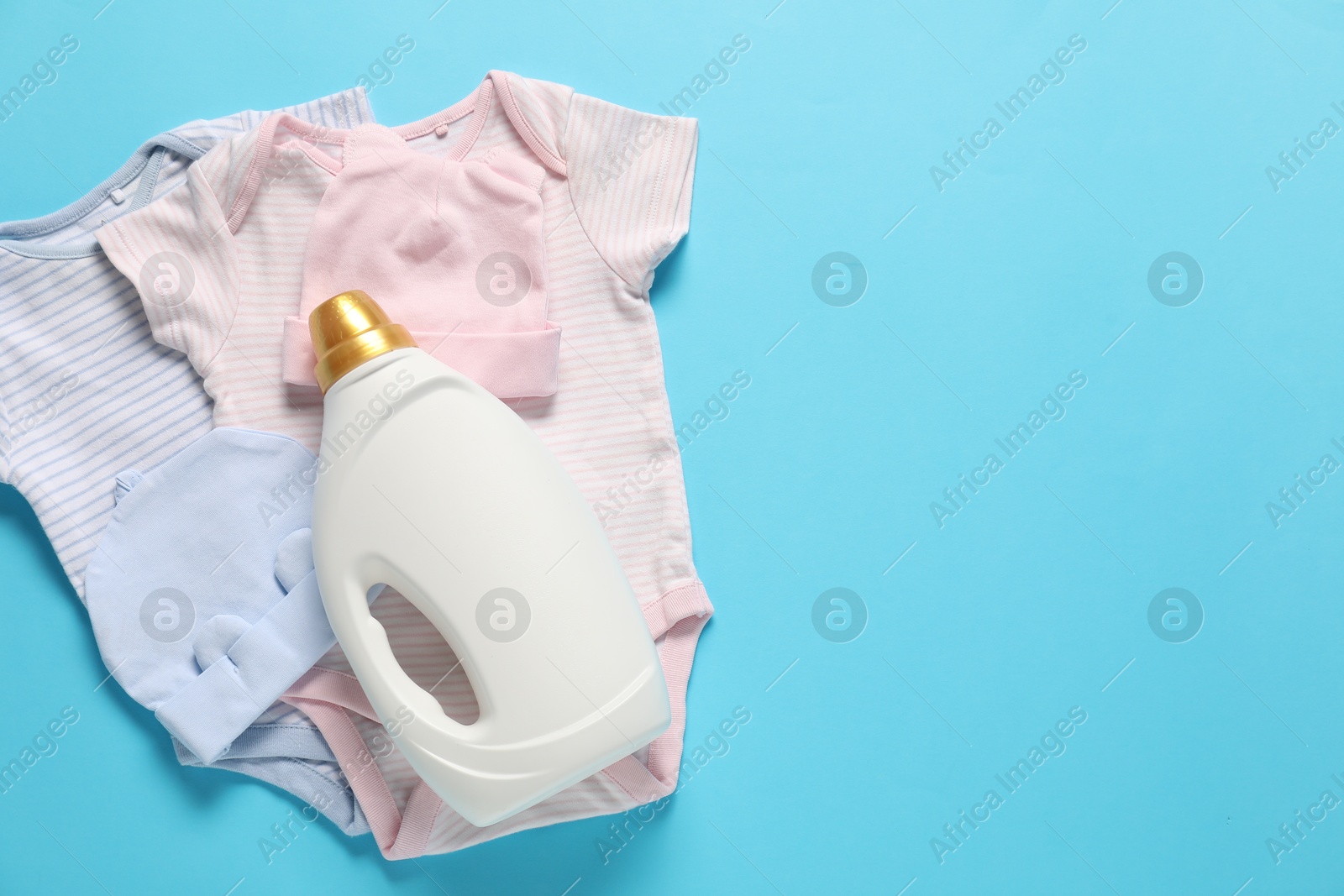 Bottle of fabric softener and baby clothes on light blue background, flat lay. Space for text Photo of Bottle of fabric softener and baby clothes on light blue background, flat lay. Space for text