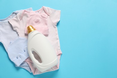 Photo of Bottle of fabric softener and baby clothes on light blue background, flat lay. Space for text