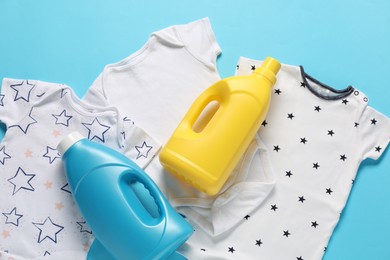 Photo of Bottles of fabric softener and baby clothes on light blue background, flat lay