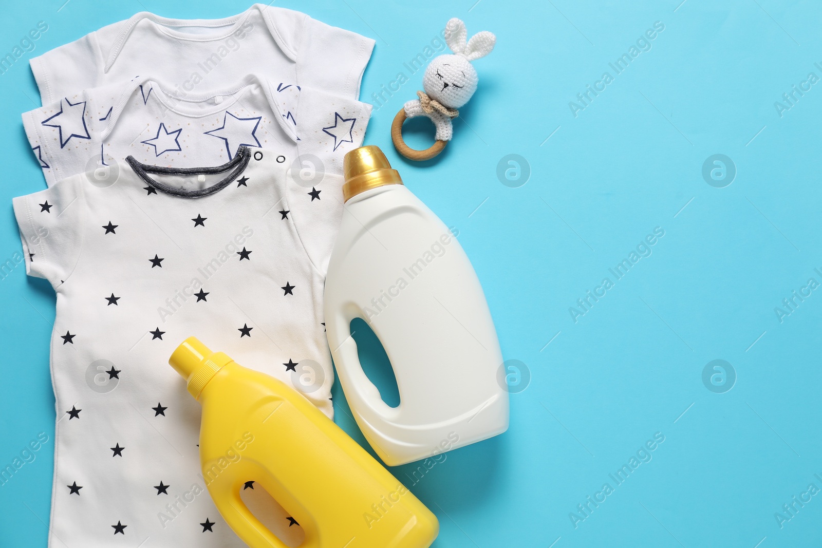 Bottles of fabric softener, toy and baby clothes on light blue background, flat lay. Space for text Photo of Bottles of fabric softener, toy and baby clothes on light blue background, flat lay. Space for text