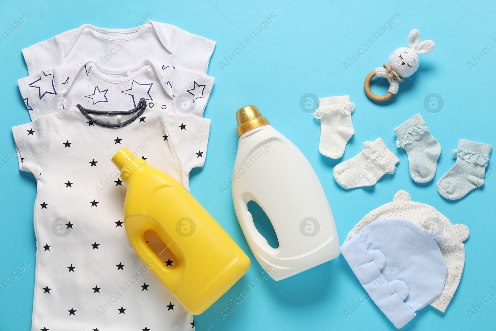 Bottles of fabric softener, toy and baby clothes on light blue background, flat lay Photo of Bottles of fabric softener, toy and baby clothes on light blue background, flat lay