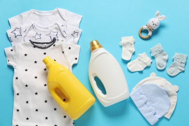 Photo of Bottles of fabric softener, toy and baby clothes on light blue background, flat lay