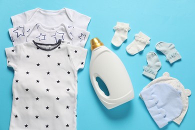 Photo of Bottle of fabric softener and baby clothes on light blue background, flat lay