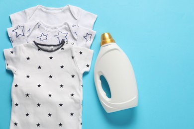Photo of Bottle of fabric softener and baby clothes on light blue background, flat lay. Space for text