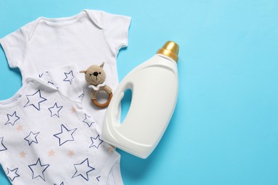 Photo of Bottle of fabric softener, toy and baby clothes on light blue background, flat lay