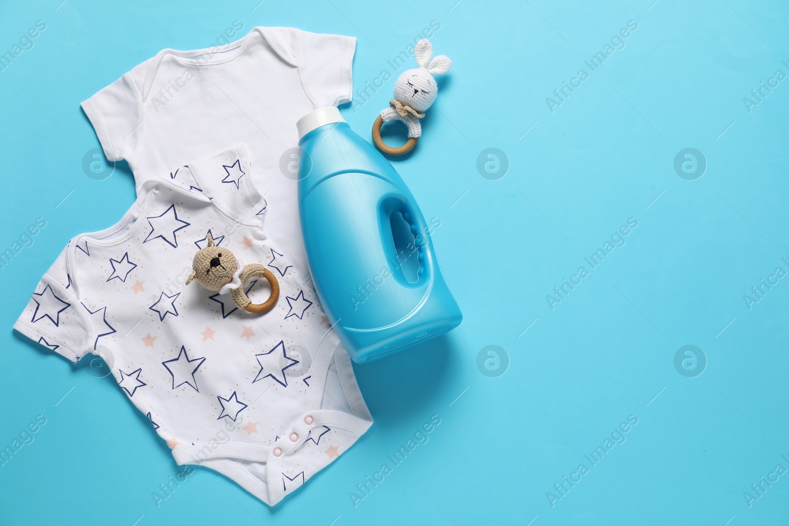 Bottle of fabric softener, toys and baby clothes on light blue background, flat lay. Space for text Photo of Bottle of fabric softener, toys and baby clothes on light blue background, flat lay. Space for text