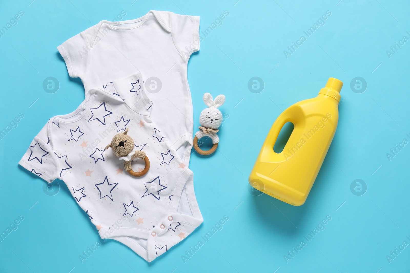Bottle of fabric softener, toys and baby clothes on light blue background, flat lay Photo of Bottle of fabric softener, toys and baby clothes on light blue background, flat lay